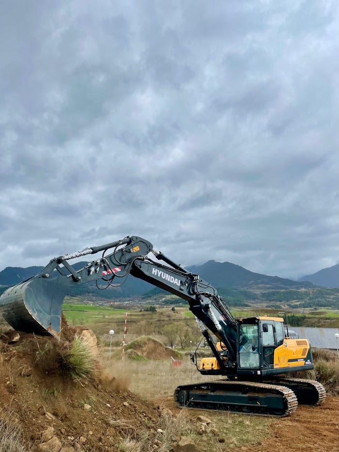 Heavy machinery excavator working at a construction site in Bolvir, Spain with scenic mountain backdrop.